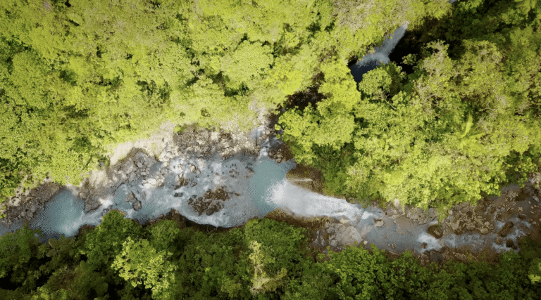 Overhead shot showcasing a winding river in the Bajos del Toro region, with a waterfall tumbling into a rocky stream hidden within the forest.