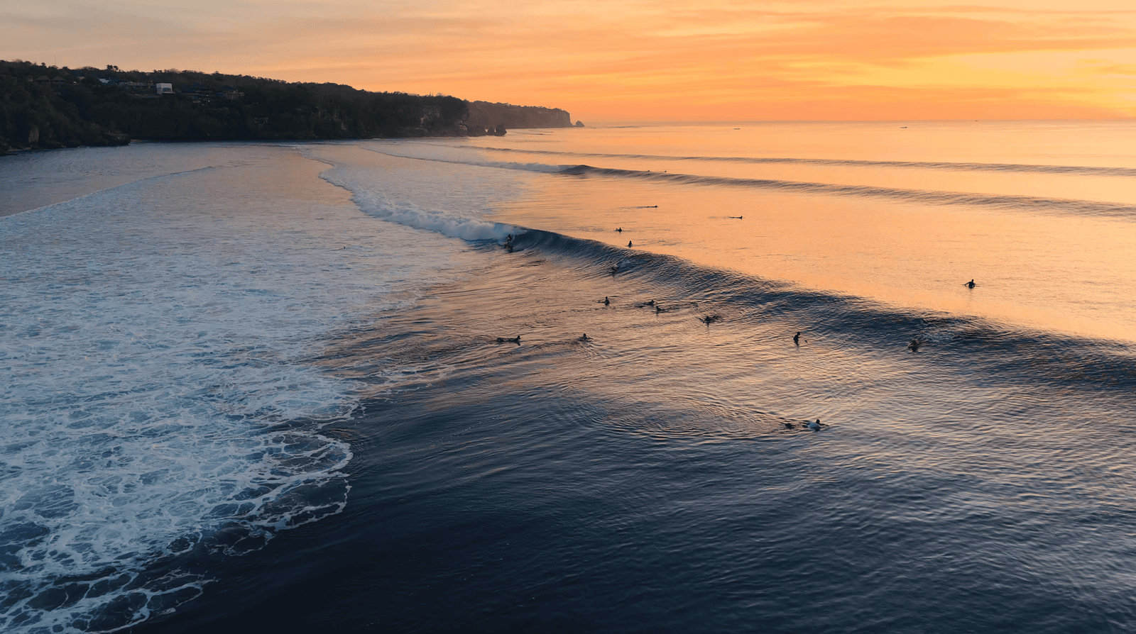 Impossible Beach Uluwatu: Worth a visit in 2026? 2 Sunset over Impossible Beach with surfers riding gentle waves along the rugged coastline.