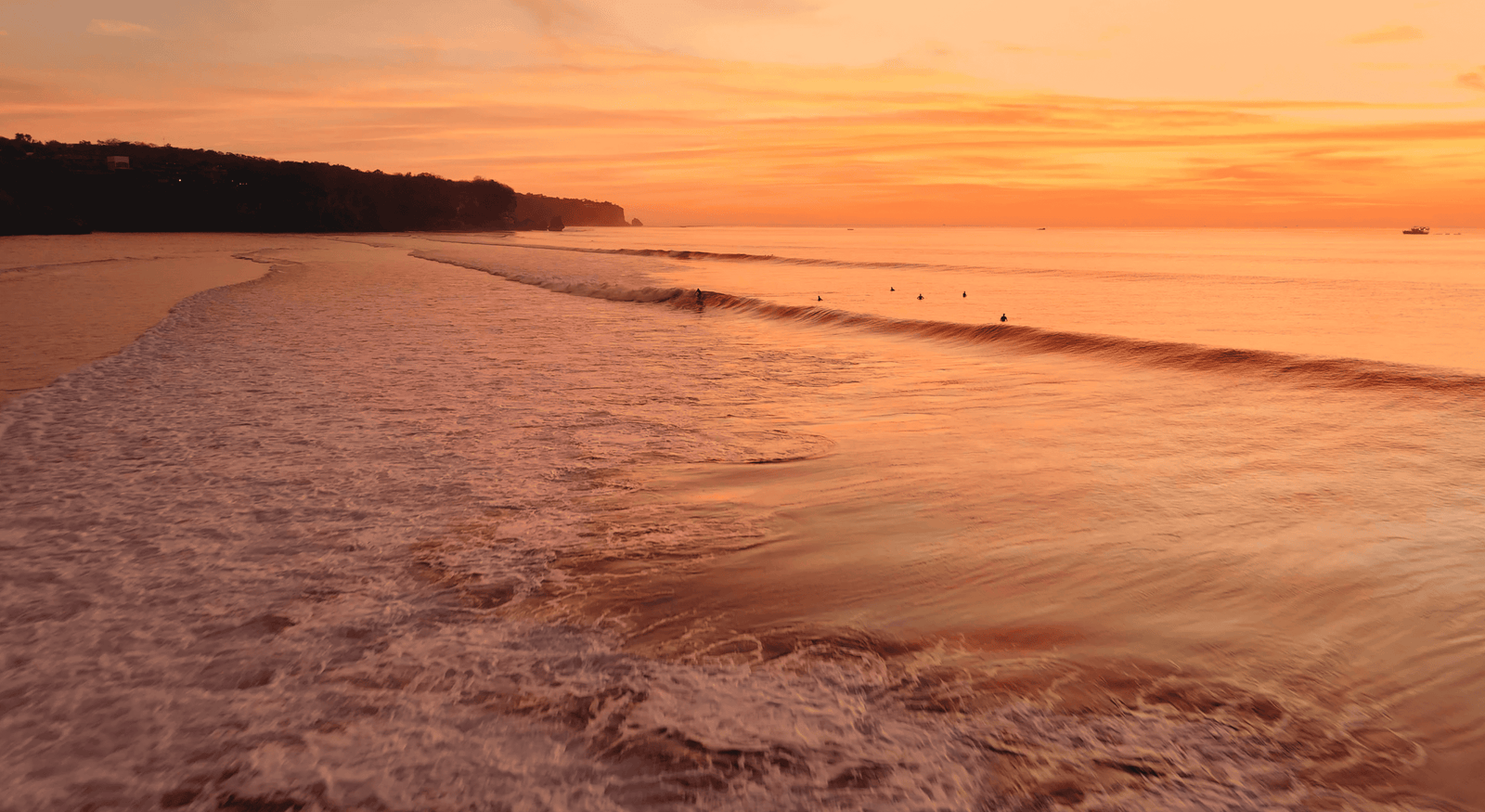 Impossible Beach Uluwatu: Worth a visit in 2026? 3 Sunset over Impossible Beach with surfers riding gentle waves along the rugged coastline.