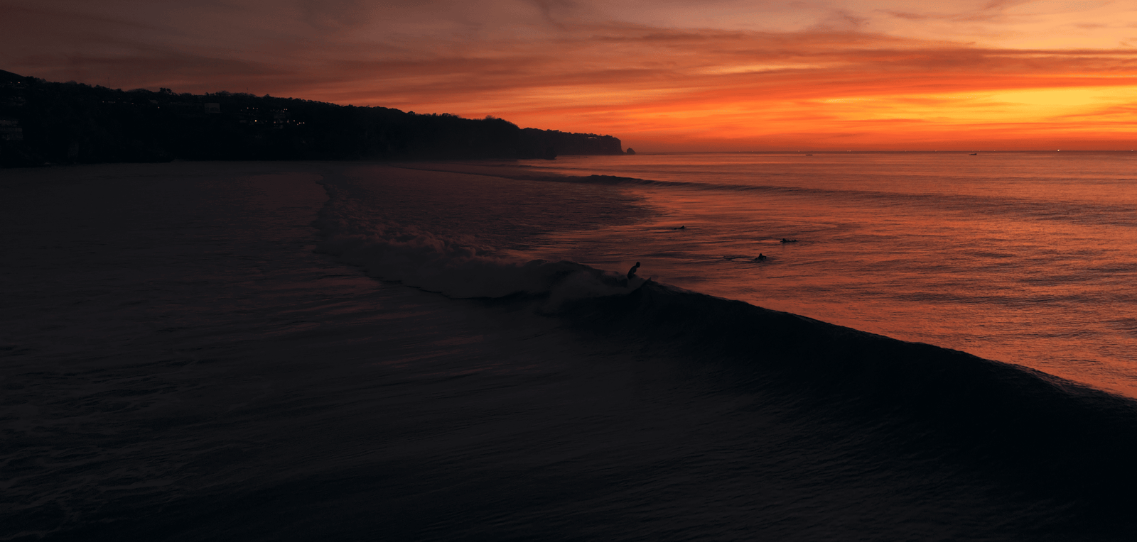 Impossible Beach Uluwatu: Worth a visit in 2026? 5 Sunset over Impossible Beach with surfers riding gentle waves along the rugged coastline.