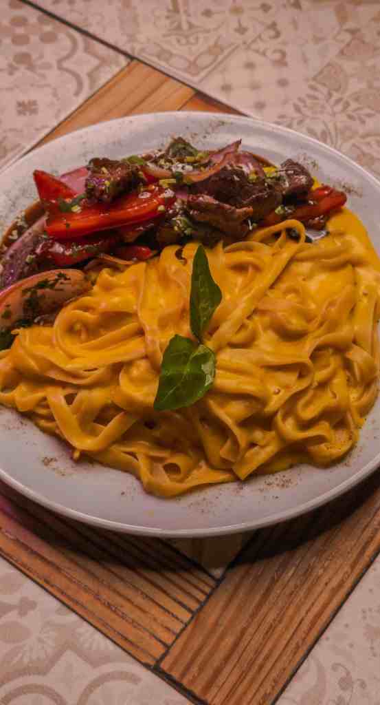 A charming, rustic restaurant featuring outdoor seating, wooden accents, potted plants, and signage offering coffee, desserts, pizza, and more, ideal for relaxing meals and social gatherings.