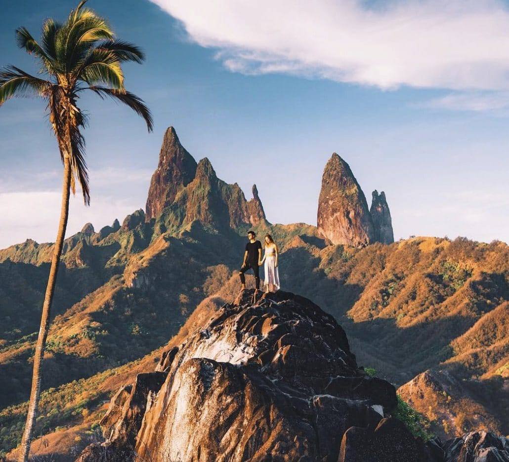 Ua Pou Marquesas Islands: A Full Guide For First-Timers 1 a man and woman standing on a rock with a palm tree and mountains in the background in Ua Pou!