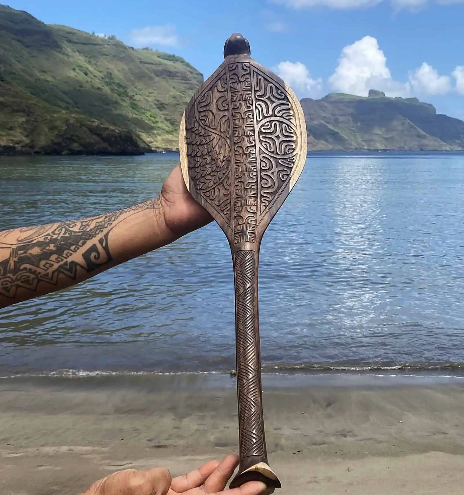 A person holding a carved wooden object on a beach