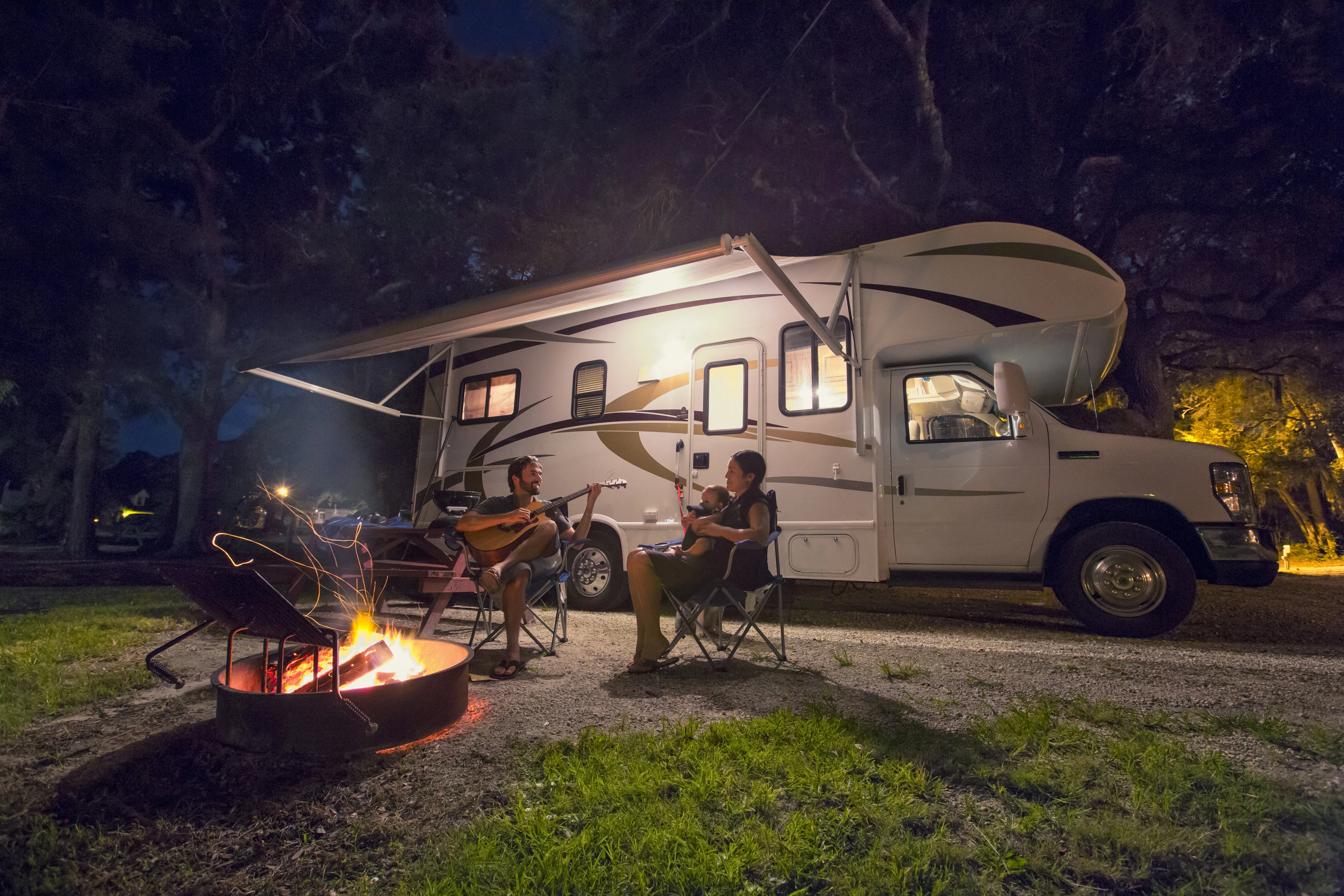 Mid adult couple and baby daughter sitting in front of campfire at night
