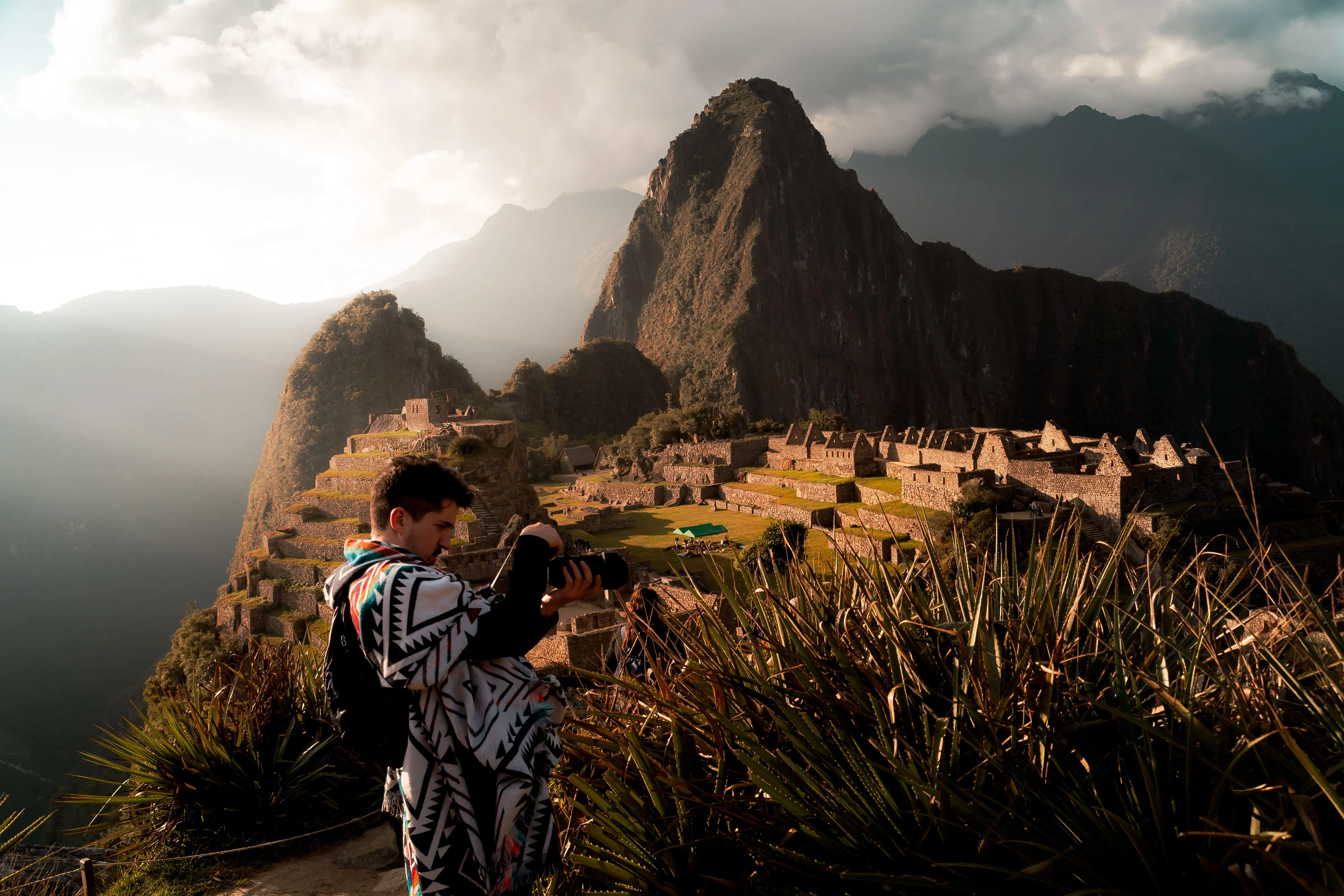 A photographer capturing the breathtaking view of Machu Picchu in Peru during sunset with a mountain backdrop.