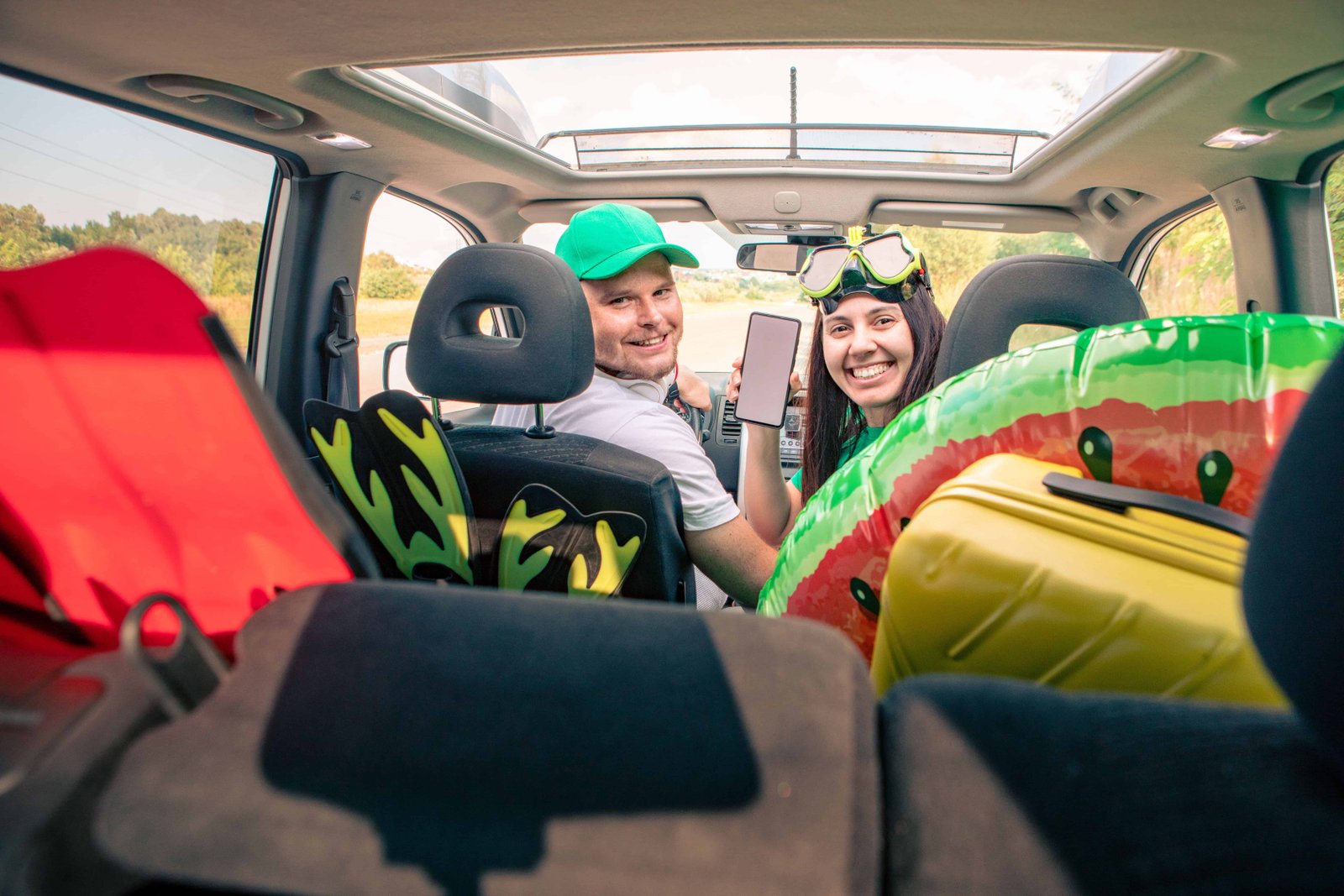 The Ultimate Guide to Road Trip Accessories for Couples 10 smiling happy couple in car holding phone with white screen sea vacation stuff