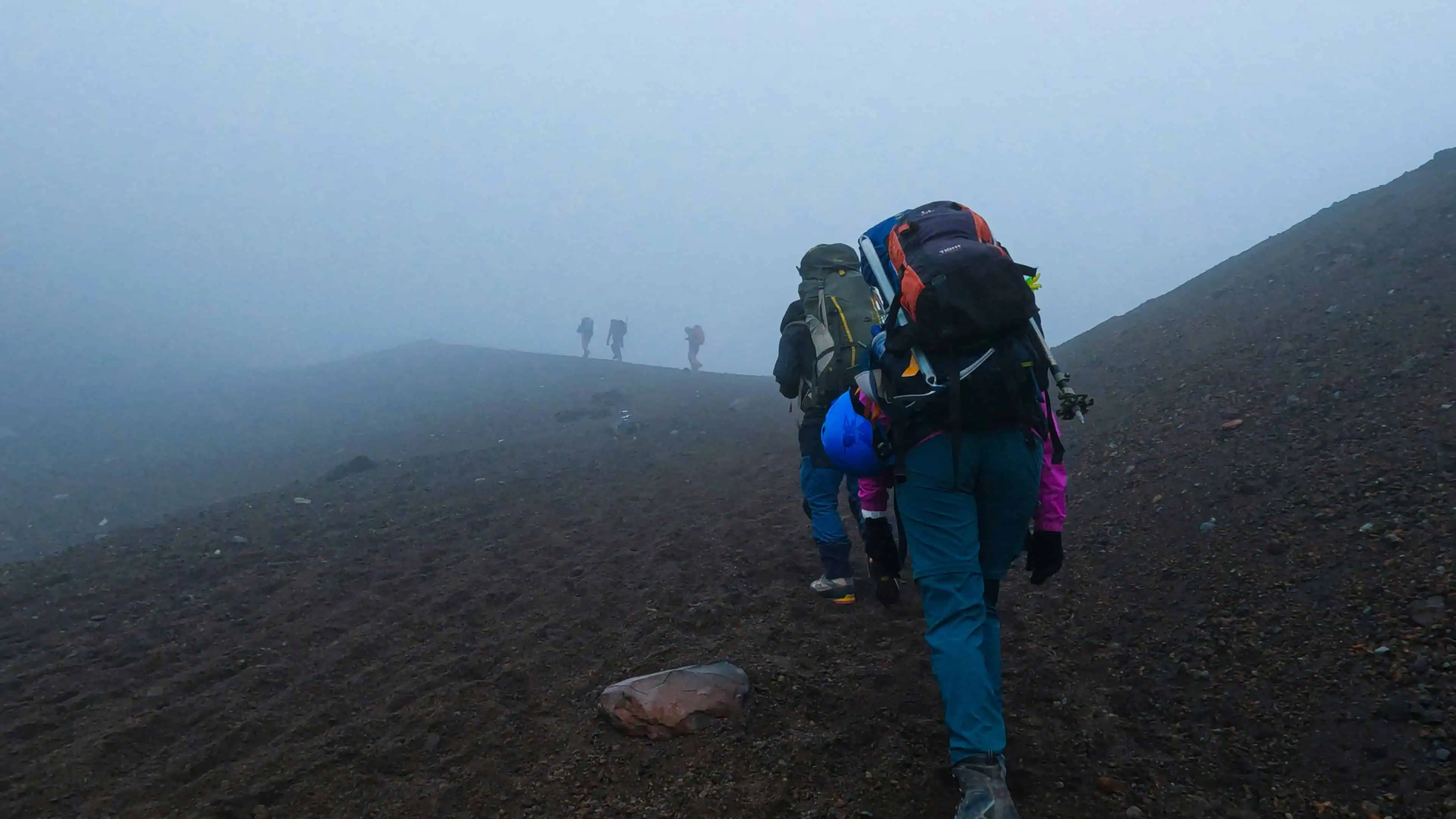Backpacking hike on a foggy mountain trail, with a group of adventurers trekking through volcanic terrain, carrying gear and backpacks for outdoor exploration and adventure.