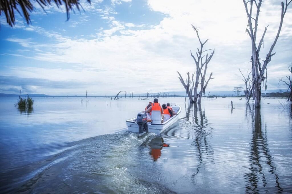 Best hotels in Naivasha Kenya: 11 picks by budget and vibe (2026 Guide) 13 A boat with travelers navigating a flooded landscape at Lake Naivasha with leafless trees and cloudy skies, capturing the mysterious and atmospheric scenery of Lost Between Oceans.