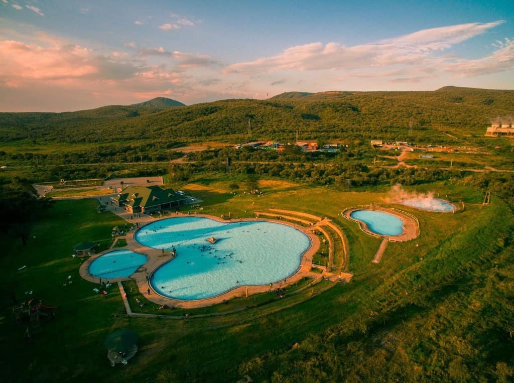 Naivasha in Kenya Travel Guide (With Itinerary and Tips) for 2026! 25 1. Aerial view of a scenic outdoor swimming pool complex surrounded by lush green hills and mountains at sunset.