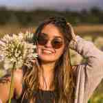 1. Smiling woman in sunglasses holding white flower outdoors on sunny day, representing nature, happiness, and freedom in scenic landscape.