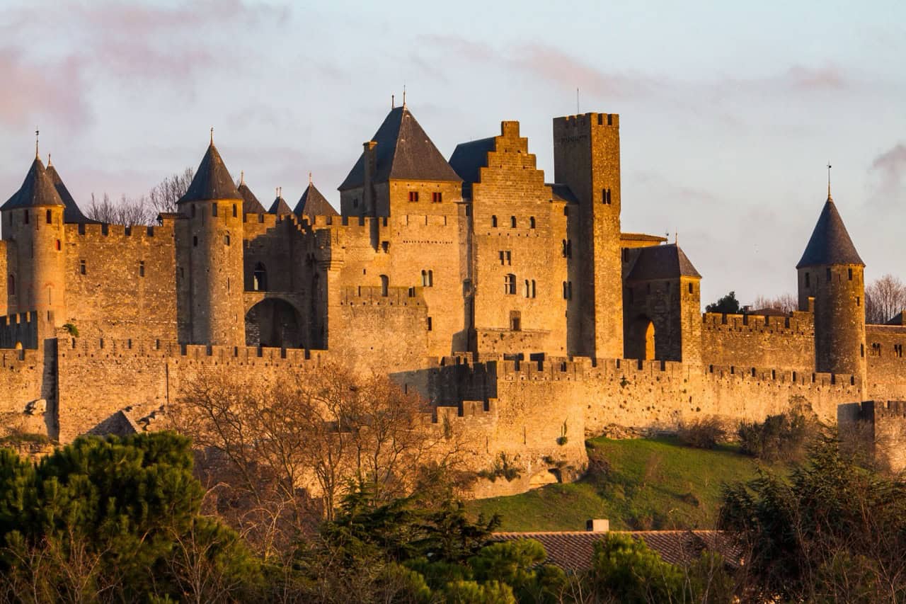 Ancient medieval castle in Carcassonne with stone walls and turrets at sunset, located in France, exemplifying historical architecture and fairy-tale castles.