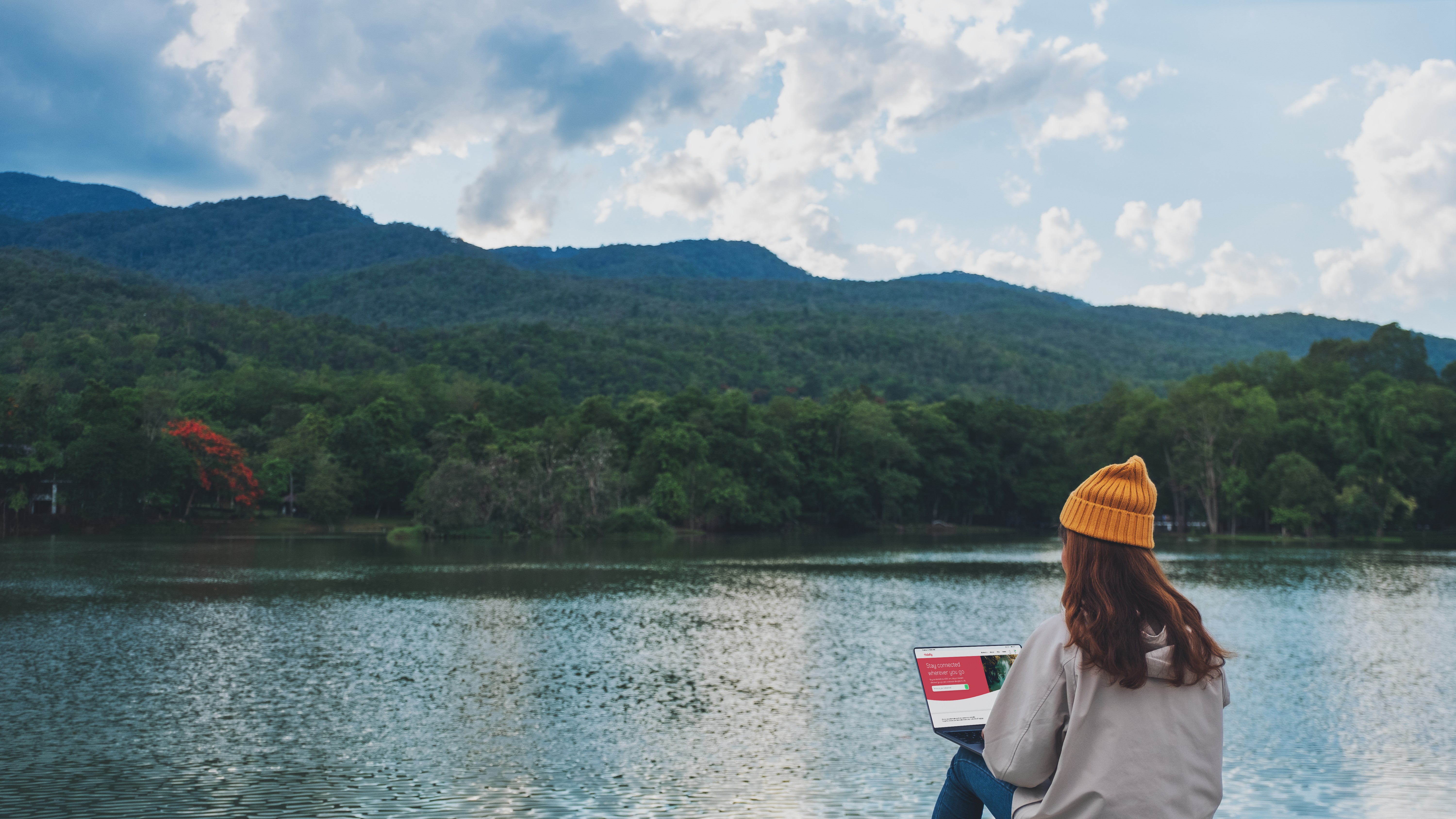 Person using Holafly on laptop in front of a lake with mountains in the background