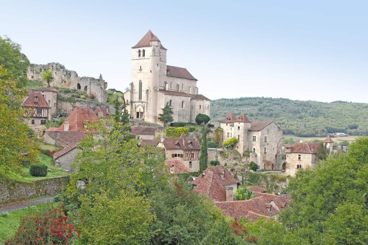 7 Charming Medieval Villages in France (2026 Expert Guide) 12 Medieval SAINT CIRQ LAPOPIE with historic castle on hill, lush greenery, and red-tiled rooftops, in a serene countryside setting.